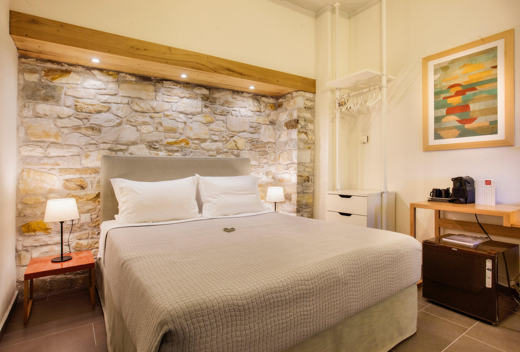 Δωμάτιο με γήινες αποχρώσεις, πέτρινο τοίχο, λεπτομέρειες από φυσικό ξύλο και κρεβάτι Cocomat. Room in earthy tones featuring a stone wall, natural wood elements, and a Cocomat bed.