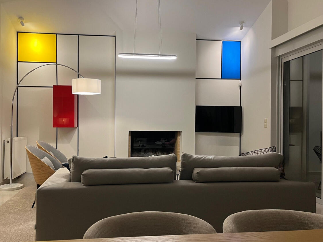 Σαλόνι μοντέρνου διαμερίσματος στην Αθήνα με τζάκι και ενσωματωμένη τηλεόραση σε τοίχο εμπνευσμένο από τον Mondrian, με καθαρές γεωμετρικές γραμμές και τολμηρά χρώματα. Modern apartment living room in Athens featuring a fireplace and integrated TV within a